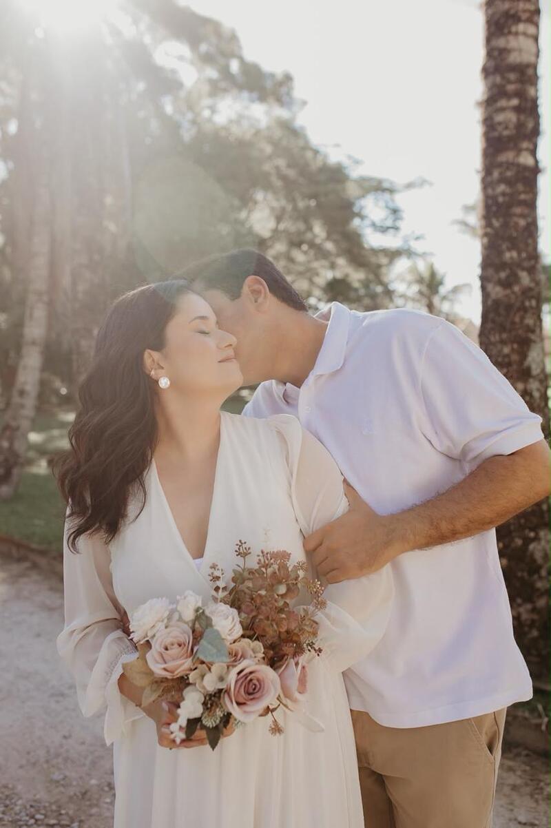 Natália e Mário se beijando ao entardecer, com buquê de flores